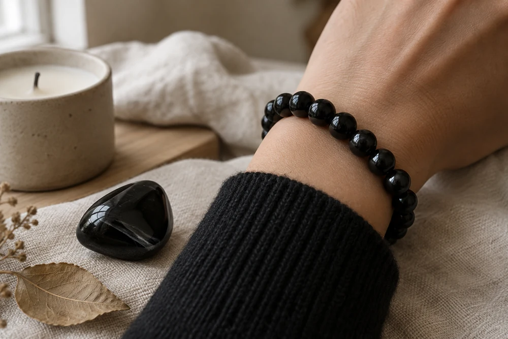 Pierre Scorpion au quotidien : bracelet en obsidienne noire porté au poignet, avec une manche de pull noir et une bougie